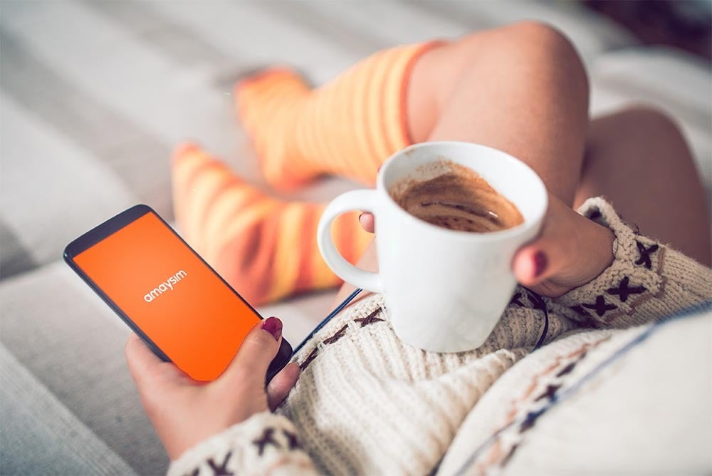 a woman drinking coffee and reading the amaysim article "10 essential apps to get you through winter"