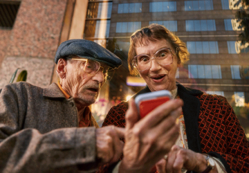 low angle shot of an older couple holding an amaysim orange backed phone and marvelling at it