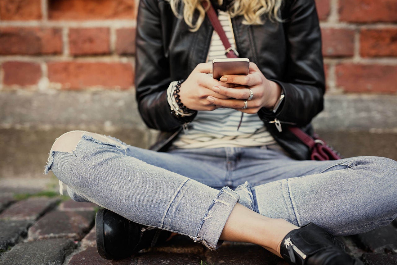 Teenage girl sitting on ground using iPhone in Australia